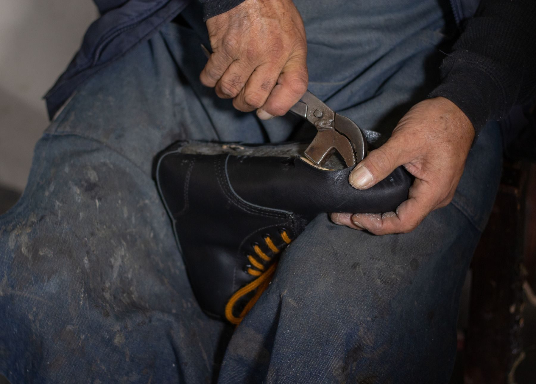 A cobbler's hands working on a black leather boot with pliers