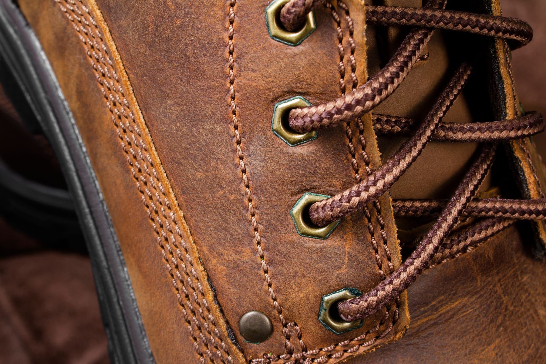 Close-up of a brown leather lace-up boot with double stitching and brass eyelets